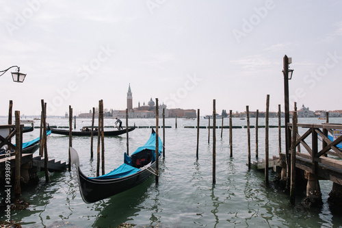 view of old wooden docks on the lake canal in venice during summer easter of boats yachts ships man working and island old town on the other side © Adam