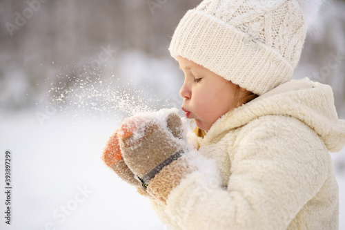 a little girl in a warm white sweater and a white hat plays with the snow during a walk in the winter forest. bright emotion.