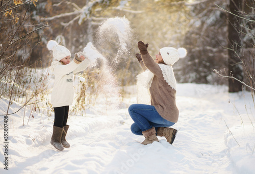 mother and daughter in warm sweaters play with snow during a walk through the winter forest. bright emotion.