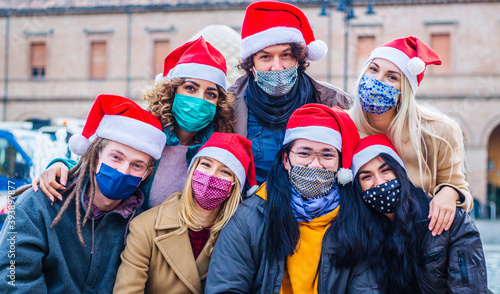 Happy people with Santa Claus hats celebrating Christmas - New normal lifestyle concept with young friends wearing face mask enjoying xmas eve.