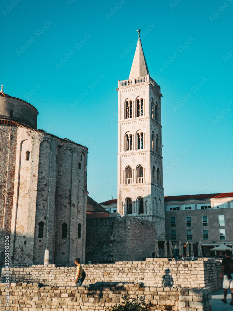 people walking around the old historic ancient ruins in front of the church of saint donatus during summer vacation in croatia