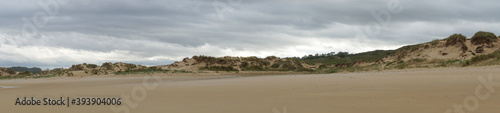 panorama of an empty beach with tall sand dunes under an overcast sky