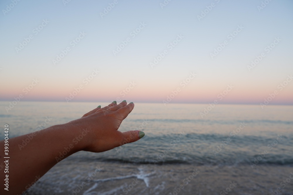 hands reaches for the sunset against the background of the sea.