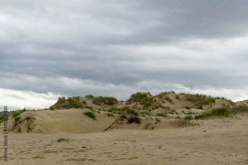 empty beach with tall sand dunes under an overcast sky