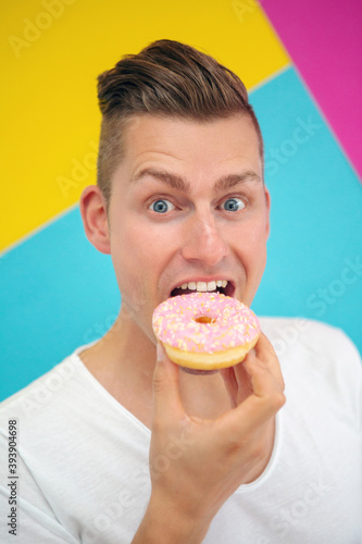 blond man on colorful background eating a pink donut