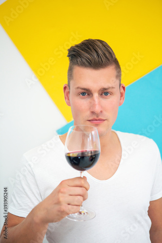 blond man holding a glass of red wine on colorful background