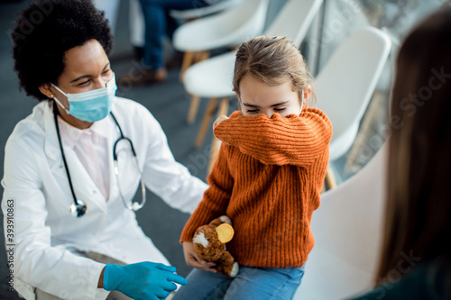 Little girl coughing into elbow while being at medical clinic. photo