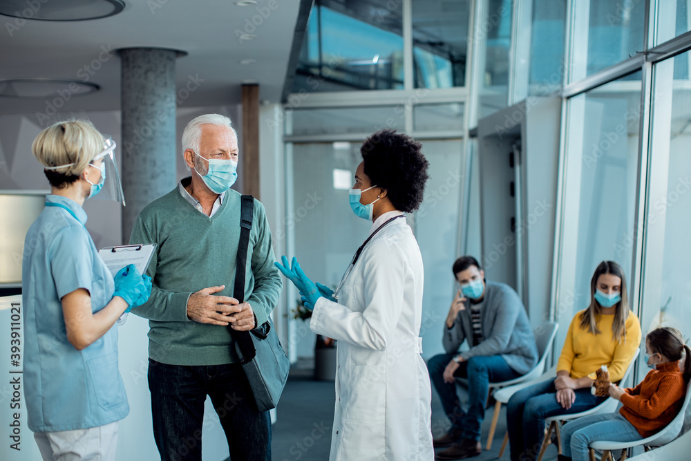 Obraz premium Senior man with protective face mask talking to doctors at hospital hallway.