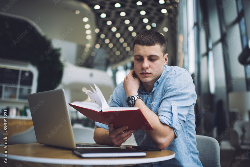 Concentrated man working on laptop and reading notebook writings at cafe table Concentrated man working on laptop and reading notebook writings at cafe table