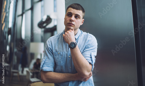 Thoughtful young man standing with arms folded and touching chin