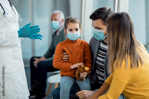 Young family wearing protective face masks while being at in waiting room at the hospital.