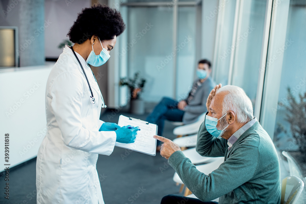 Black female doctor and senior man with face masks analyzing medical reports in a hallway at the hospital. Black female doctor and senior man with face masks analyzing medical reports in a hallway at the hospital.