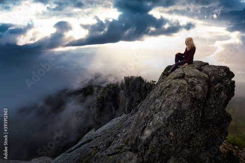 Adventurous Girl on top of a rugged rocky mountain. Dramatic Colorful Sunrise Sky Art Render. Taken on Crown Mountain, North Vancouver, BC, Canada.