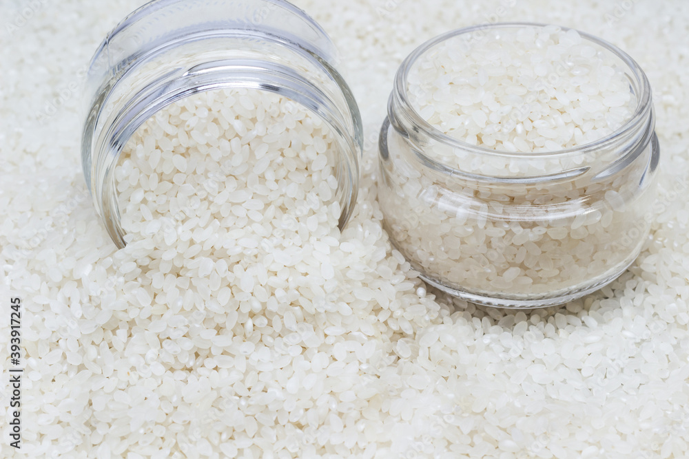 White round rice in two glass jars. Scattered rice as food background. White round rice in two glass jars. Scattered rice as food background.