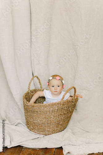 Baby girl sits and peeks out from wicker basket.