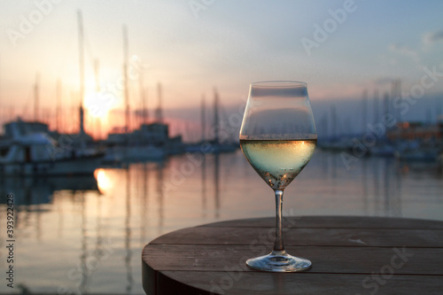 Romantic evening sunset with misty glass of white wine on background sea and yacht club.