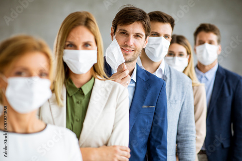 Business man taking off hisprotective facial mask and looking at the camera with histeam members standing in the line