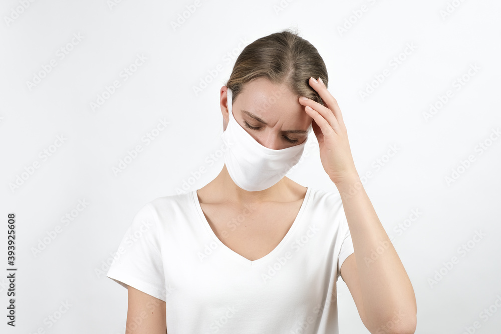 Young blond woman in virus disposable face mask  keeping raised hand on her head expressing feelings, sadness, worried. Protection for covid-19