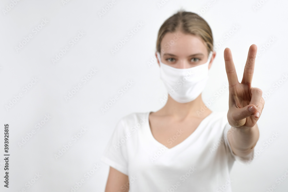 Young caucasian woman in face disposable mask showing victory sign, peace symbol. Isolated, standing in front of the white background. Young caucasian woman in face disposable mask showing victory sign, peace symbol. Isolated, standing in front of the white background.