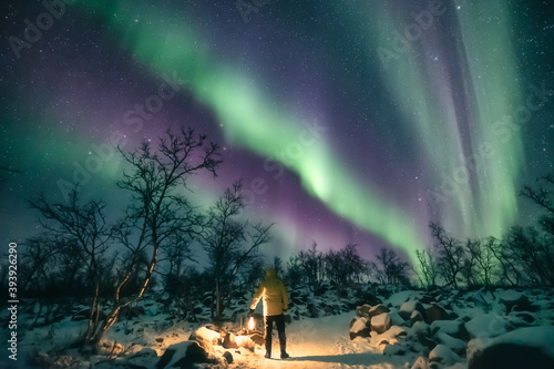 Man holding a lantern and watching northern lights in snowy scenery