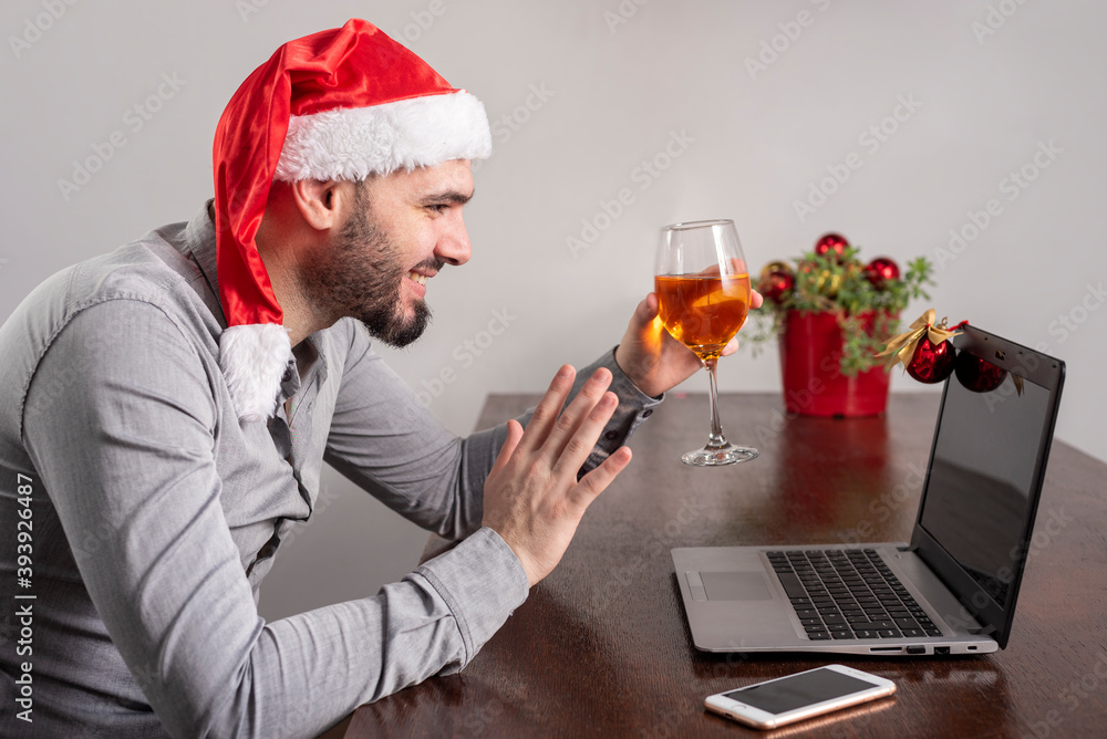 young man with Christmas hat toasting through laptop and cell phone celebrating Christmas online smiling and happy young man with Christmas hat toasting through laptop and cell phone celebrating Christmas online smiling and happy