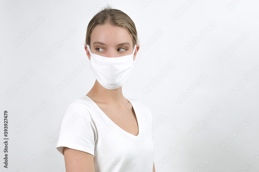 young caucasian blonde woman in disposable face protection mask points aside on free space, indoor studio photo on the white background, advertising young caucasian blonde woman in disposable face protection mask points aside on free space, indoor studio photo on the white background, advertising