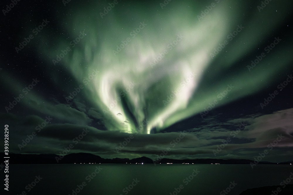 Hear-shaped aurora behind clouds in a fjord landscape