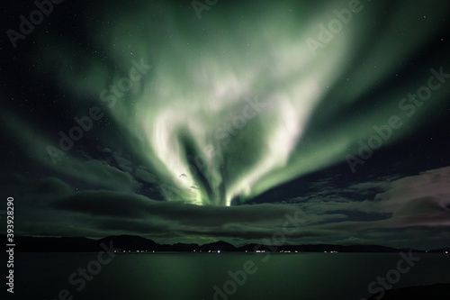 Hear-shaped aurora behind clouds in a fjord landscape photo