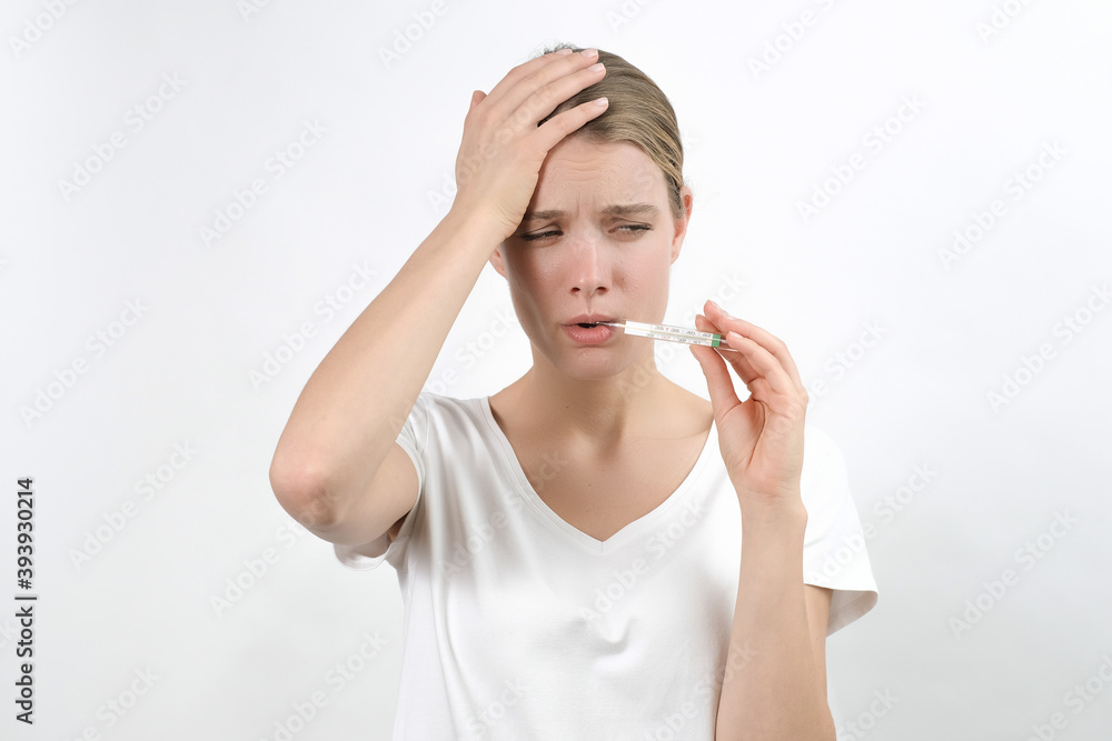 Φωτογραφία young caucasian blonde woman holding a thermometer in her mouth and keeping raised hand on her head and frowning sadly face, isolated on the white background