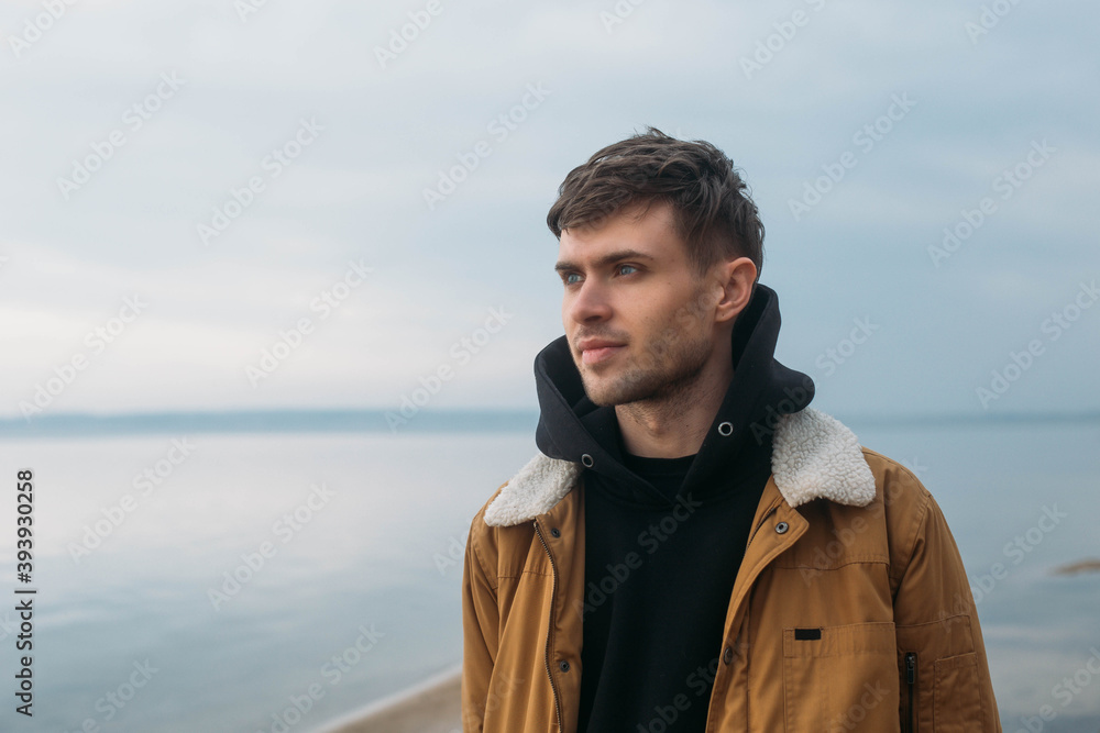 Portrait of a young guy in a yellow jacket against the background of the lake and the sky in a semi-profile. Portrait of a young guy in a yellow jacket against the background of the lake and the sky in a semi-profile.