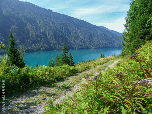 A gravelled road going along the Weissensee lake in Austria. The sides of the road are overgrown with wild flowers and tall grass. High Alps. Exploration and discovery. Beauty of the nature photo