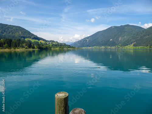 An idyllic view on the Weissensee lake in Austria. The lake is surrounded by high Alps. The calm water reflects the mountains on it's surface. Few clouds above the peaks. Calmness and peace photo