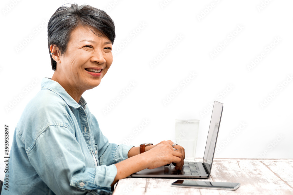 Happy Senior businesswoman working on a laptop in office. Asian mature female smiling at a laptop computer while sitting at her desk. Isolated white background. Active Elderly concept Happy Senior businesswoman working on a laptop in office. Asian mature female smiling at a laptop computer while sitting at her desk. Isolated white background. Active Elderly concept