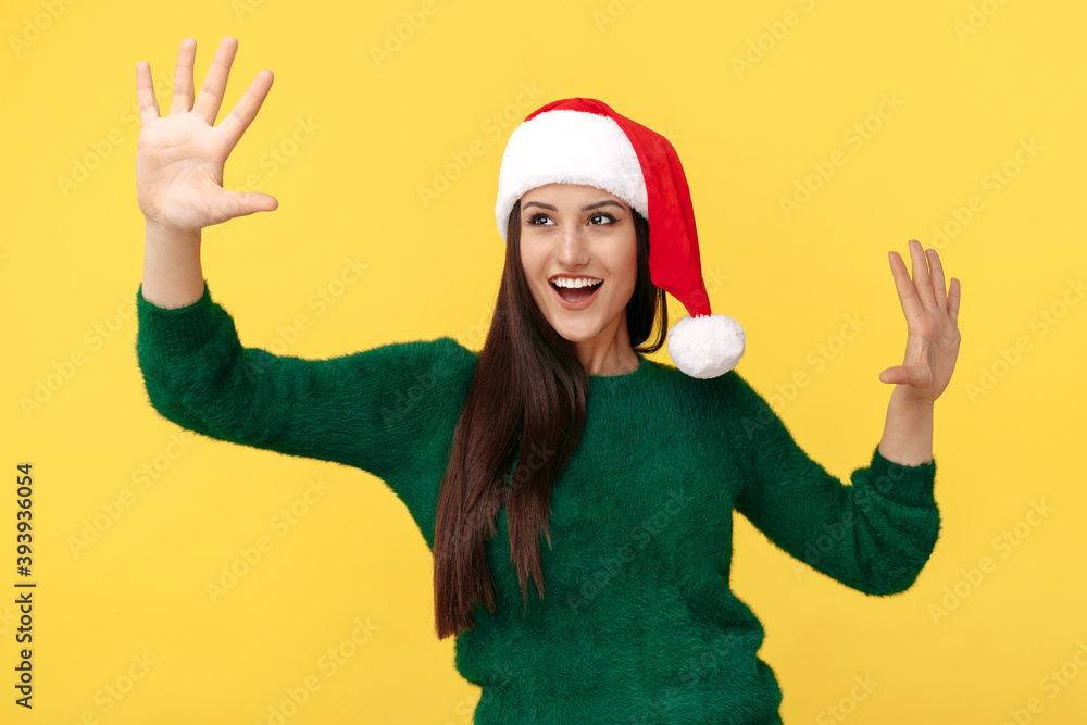 Cheerful young brunette woman wear santa claus hat and green pullover over yellow background. Cheerful young brunette woman wear santa claus hat and green pullover over yellow background.