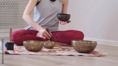 Woman playing on Tibetan singing bowl while sitting on yoga mat. Vintage tonned.