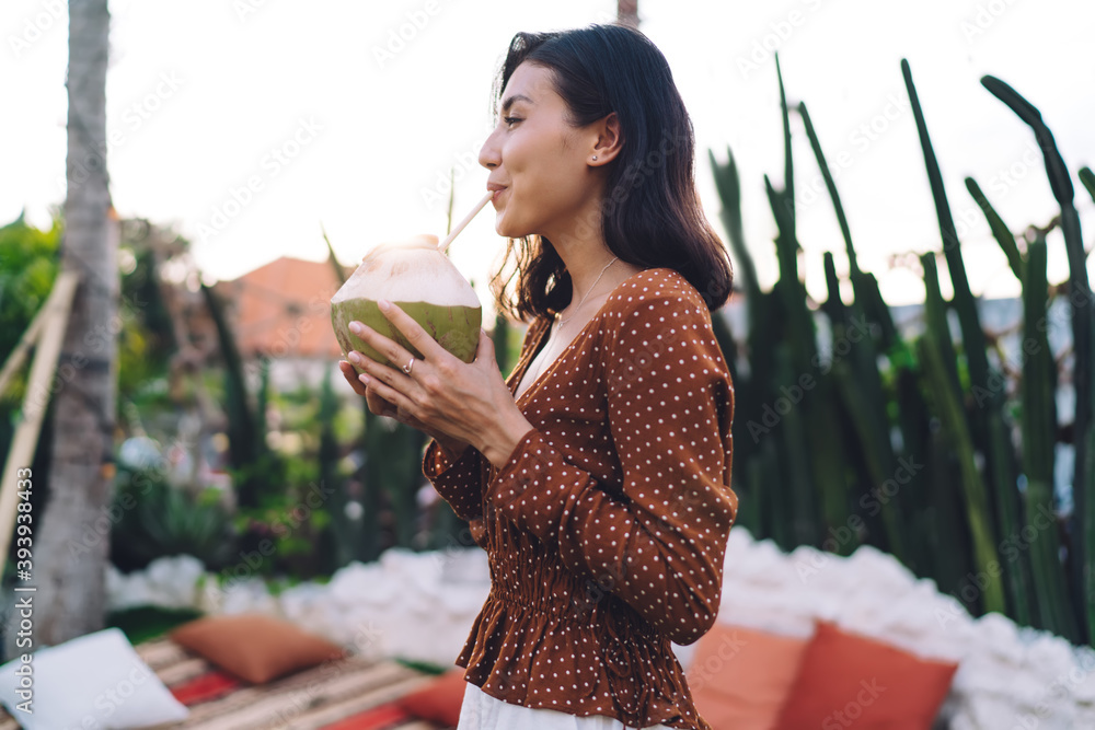 Fototapeta premium Happy young woman drinking coconut water during exotic holiday