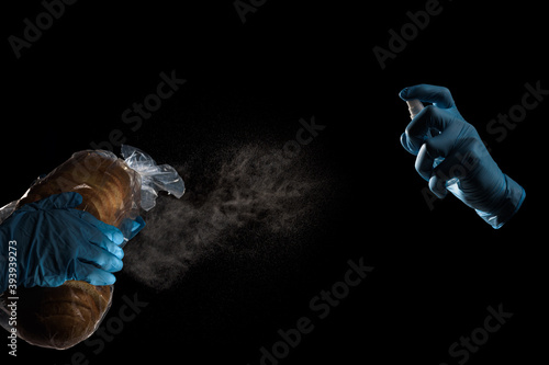 Hands in protective gloves desinfecting bread on black studio background © Denys Kurbatov