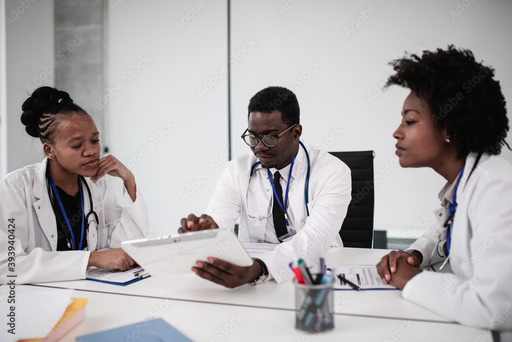 Team of three African-American doctors sitting in modern hospital and talking during business meeting.