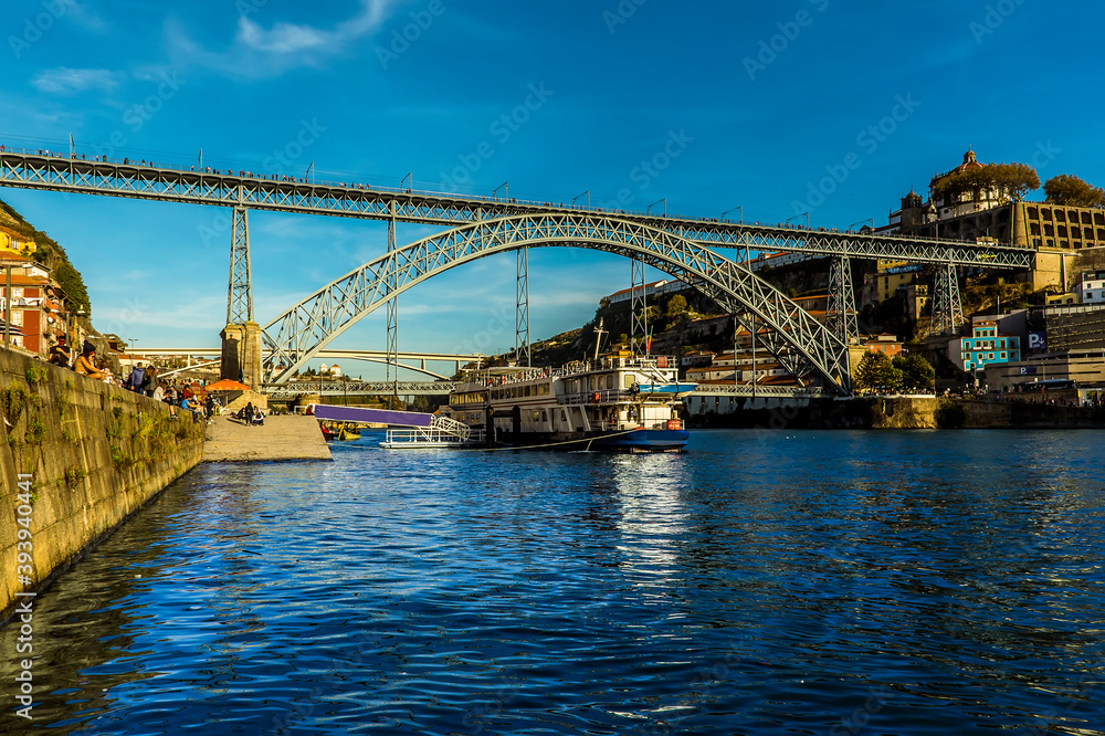 Tourist cruiser sets sail beneath the Dom Luiz bridge in Porto, Portugal on a late sunny afternoon