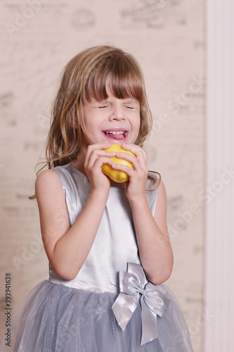 little blond baby girl eating sore lemon and grimacing on retro wall interior background