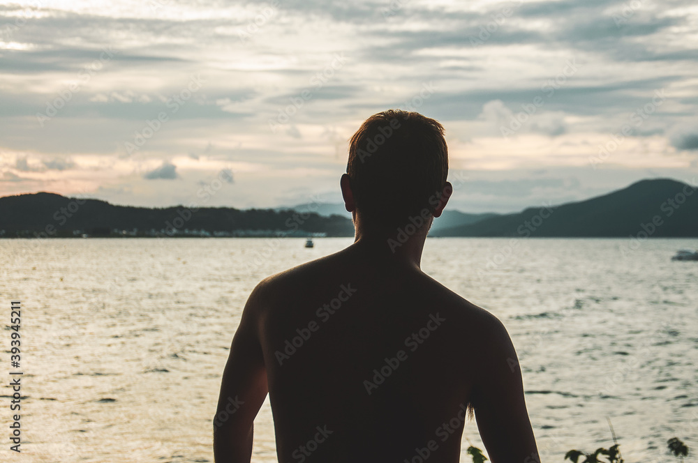 man on his back on the beach watching the sunset on the seashore, with mountains in the background