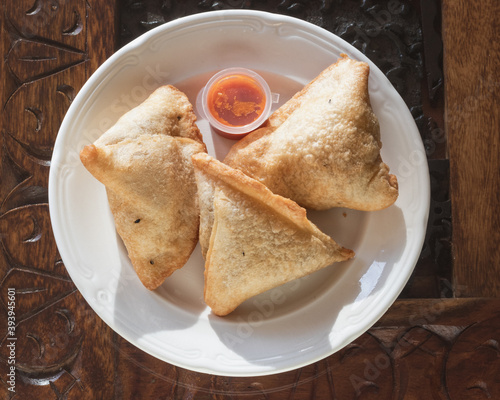 Samosas on a wooden table served with hot red sauce on white porcelain