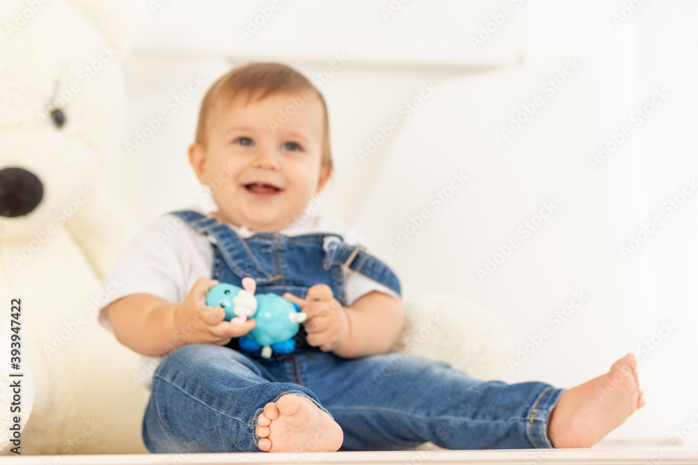 happy little baby six months old in blue jeans sits next to a large Teddy bear, legs in focus happy little baby six months old in blue jeans sits next to a large Teddy bear, legs in focus