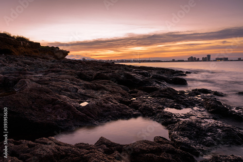 Stunning sunset from a rocky beach in Cabo de Palos with La Manga del Mar Menor skyline in the background, Murcia, Spain