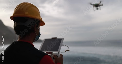 Man engineer flying with drone while wearing protective mask during coronavirus outbreak - Video surveillance and geology survey ispection concept photo