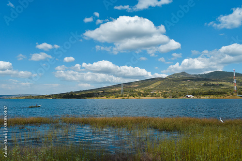 Vista de un lago con nubes  en el cielo en donde se ve un bote y una garza