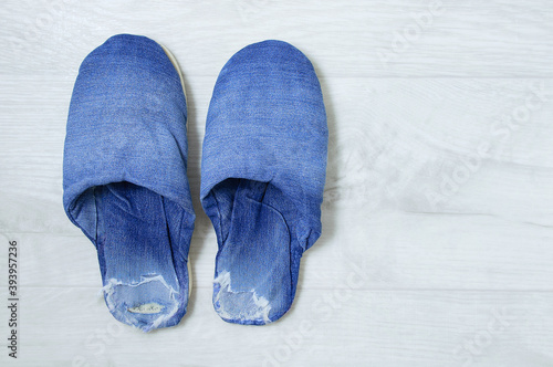Shabby ripped denim house slippers on gray wooden background.