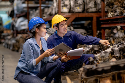 Close up Asian warehouse woman discuss together with factory worker man by sitting in automotive parts workplace area. Concept of good management and support system for industrial business. photo
