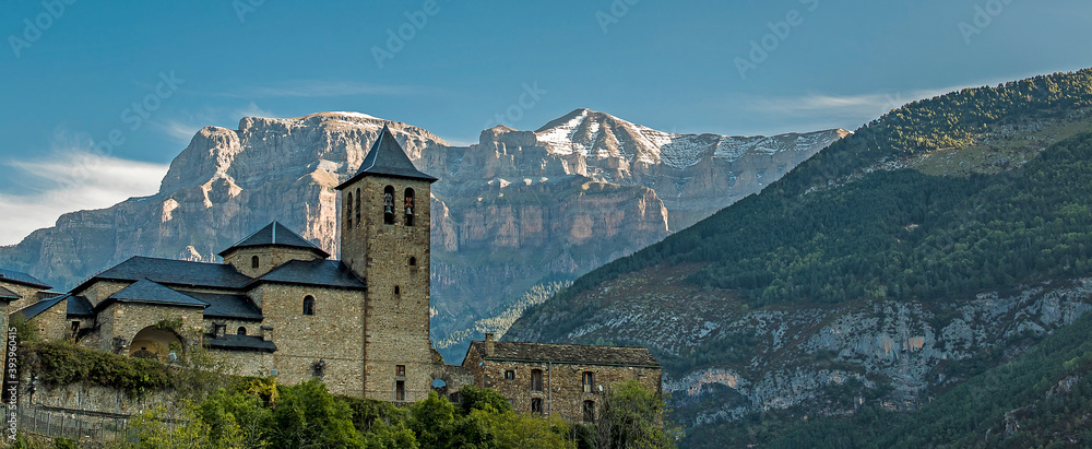 panoramic view of the church of san sebastian de torla and snow-capped mountains of the valley of ordesa in the background. Huesca pyrenees