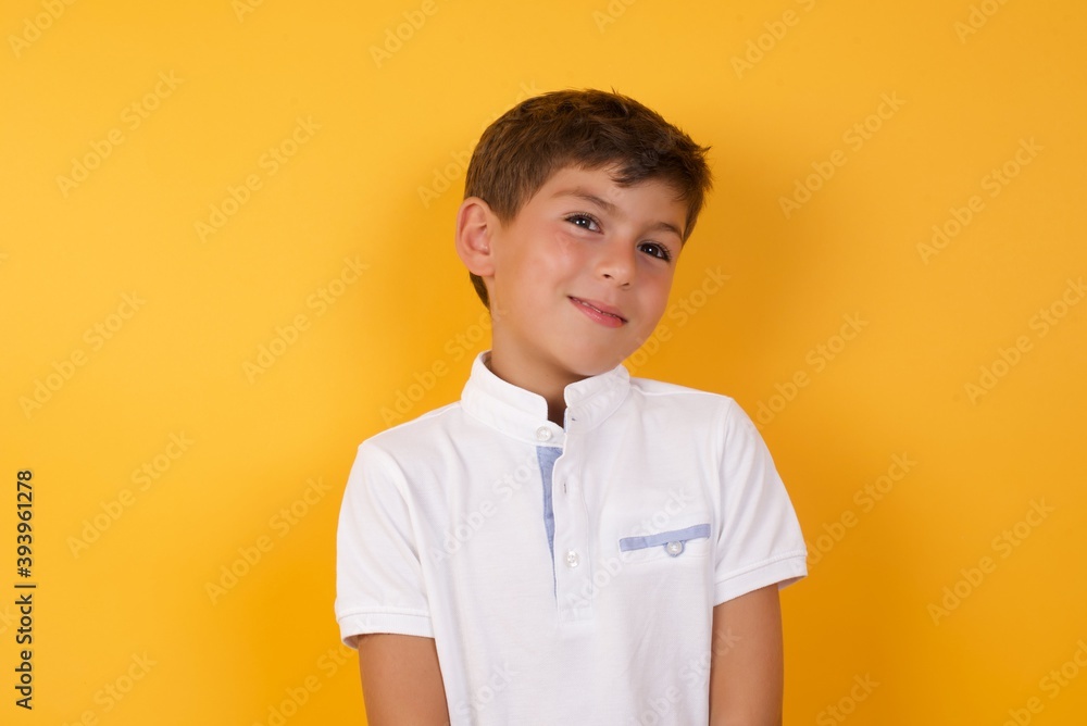 Portrait of mysterious little cute Caucasian boy kid wearing white t-shirt against yellow wall looking up with enigmatic smile. Advertisement concept. Portrait of mysterious little cute Caucasian boy kid wearing white t-shirt against yellow wall looking up with enigmatic smile. Advertisement concept.